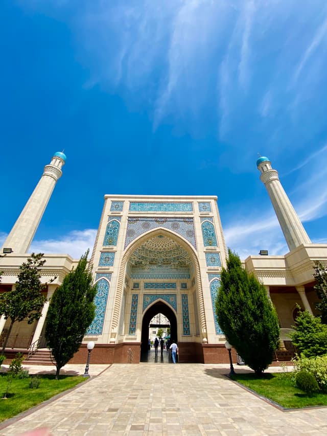 A stunning mosque entrance under a vibrant blue sky, with intricate tilework and lush greenery, exuding tranquility and architectural beauty