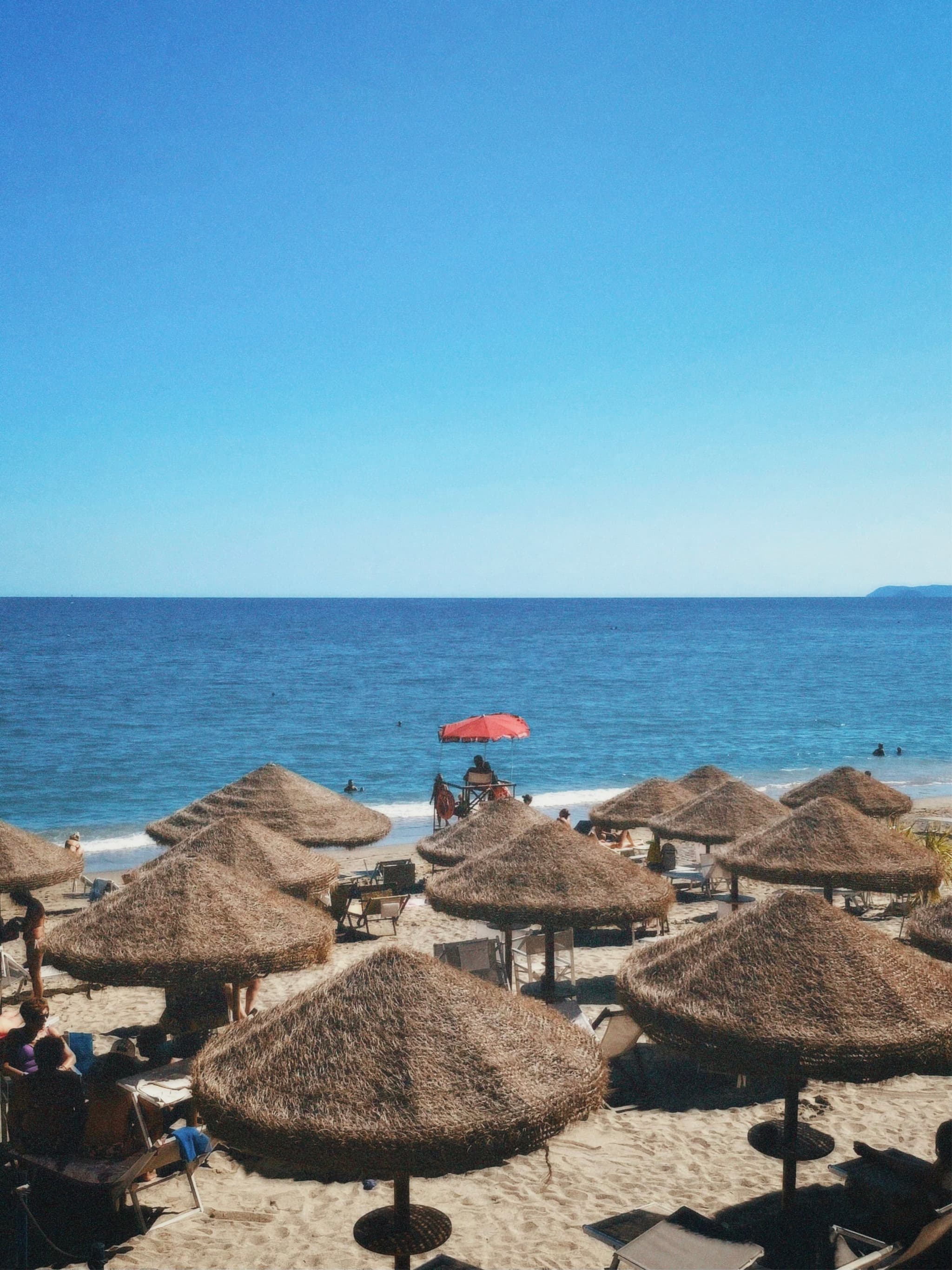 A serene beach scene with straw umbrellas, calm turquoise waters, and a clear blue sky, evoking relaxation and vacation vibes