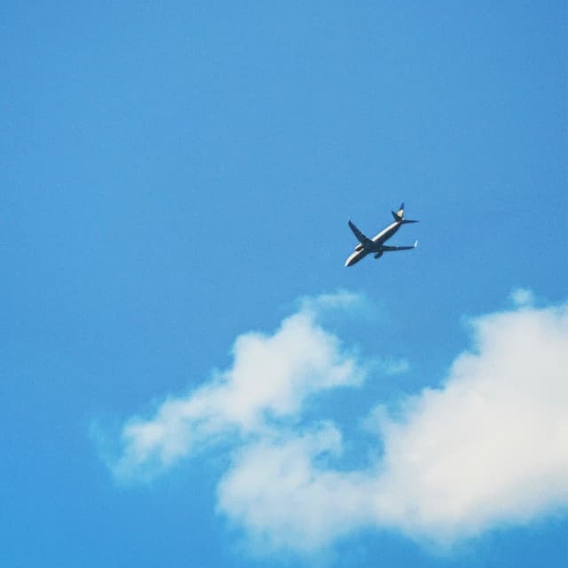 A small airplane soars through a clear blue sky with fluffy white clouds, evoking a sense of freedom and adventure