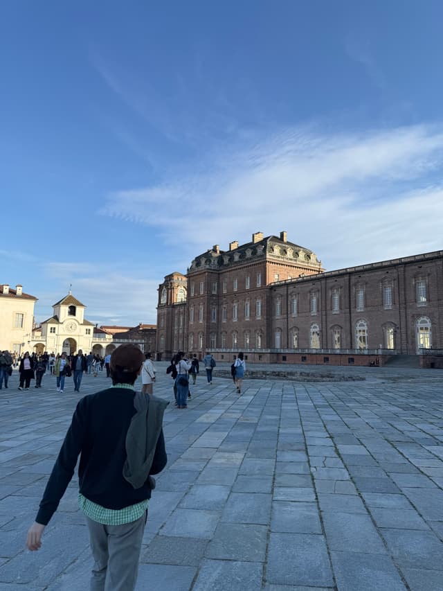A serene square scene under a clear blue sky, with a grand building and a bustling courtyard, bathed in soft, natural light