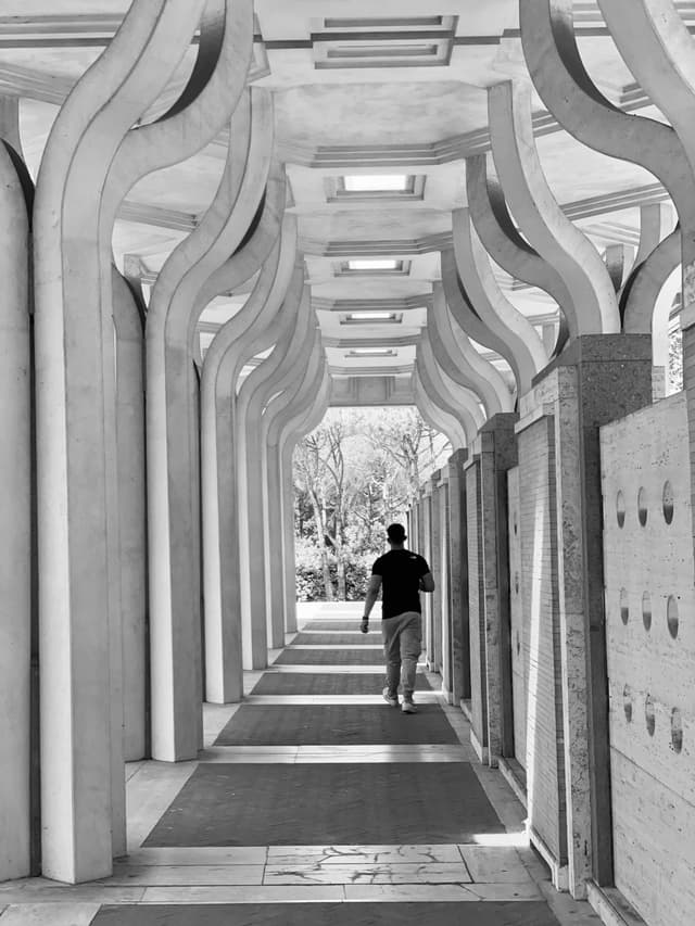 A man walks through a modern, monochrome archway, bathed in soft, natural light, creating a serene and contemplative ambiance
