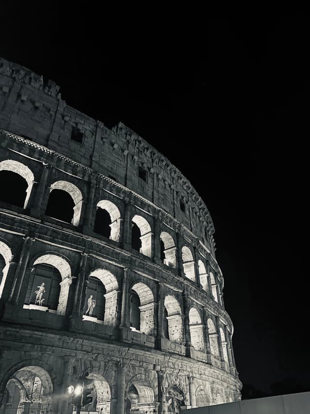 The iconic Roman Colosseum stands tall under a dark night sky, illuminated by soft lighting that highlights its ancient arches and columns, creating a dramatic and timeless atmosphere