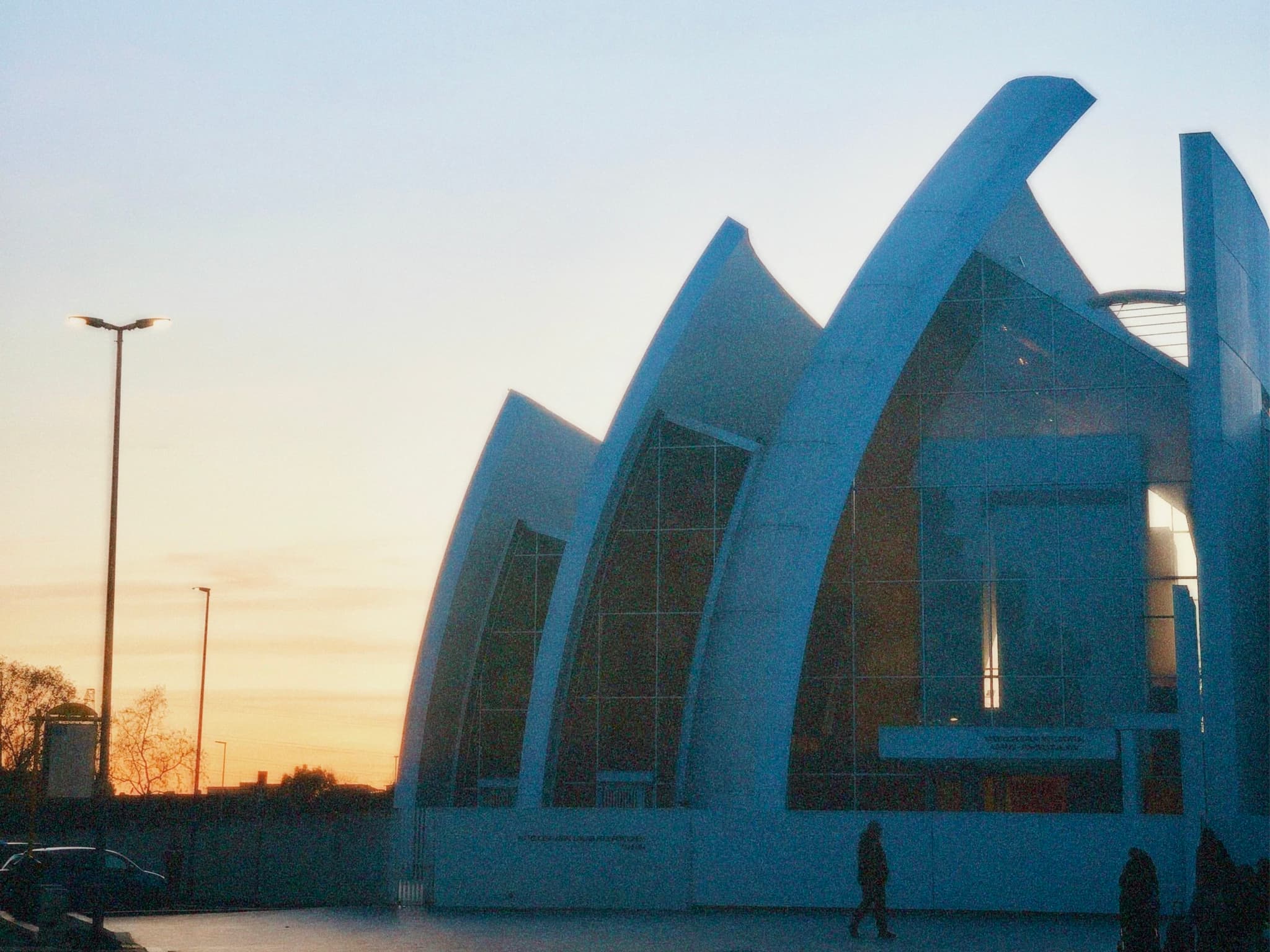A modern, abstract structure stands against a vibrant sunset sky, illuminated by soft, natural light, evoking a serene and contemplative mood