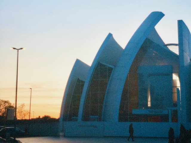 A modern, abstract structure stands against a vibrant sunset sky, illuminated by soft, natural light, evoking a serene and contemplative mood