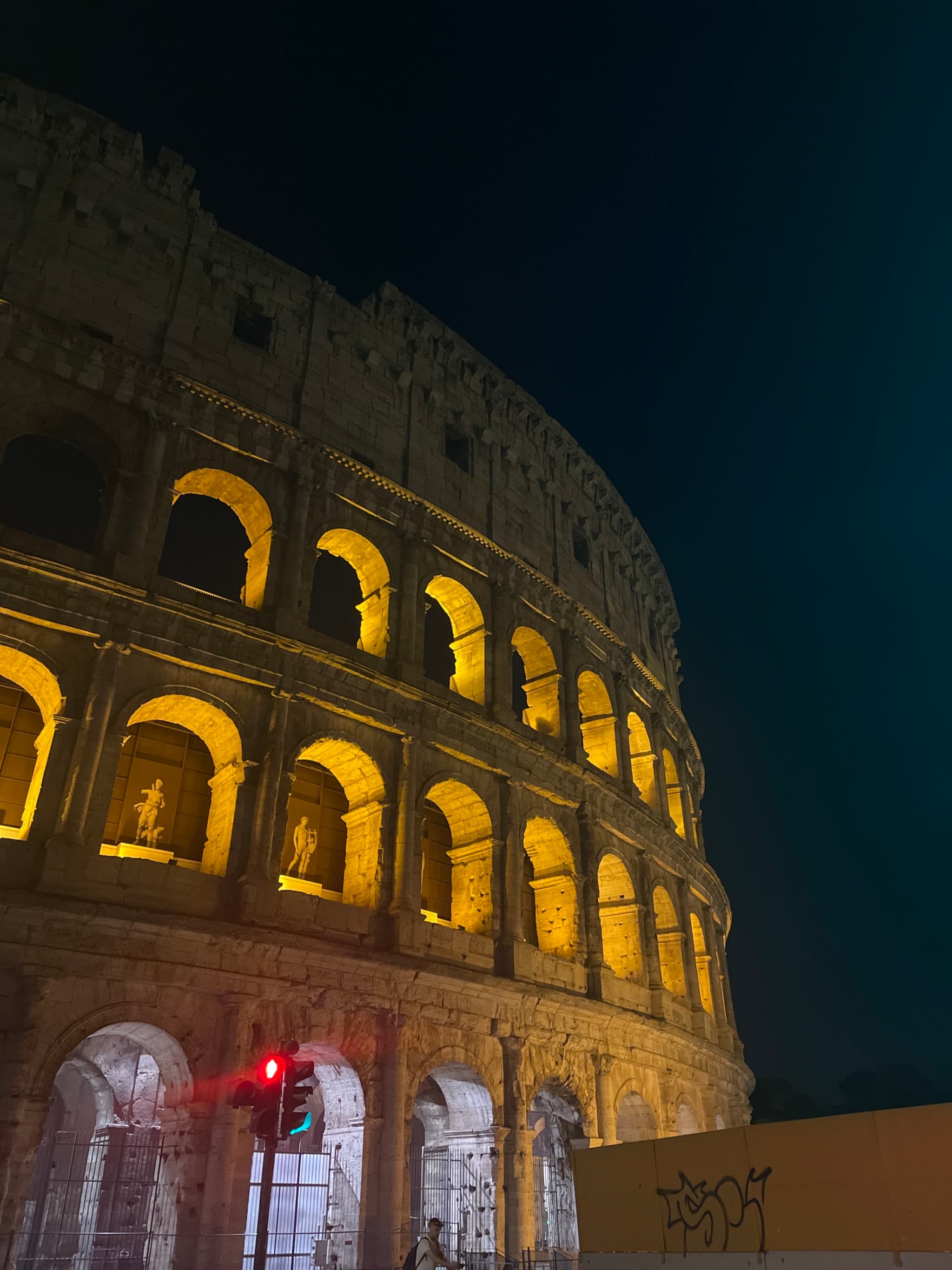 The illuminated Colosseum at night, vibrant yellow light against dark sky, evokes timeless grandeur and mystery