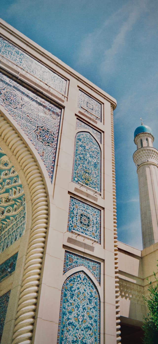 A traditional mosque with intricate tilework and a towering minaret against a clear blue sky, exuding timelessness and spiritual beauty