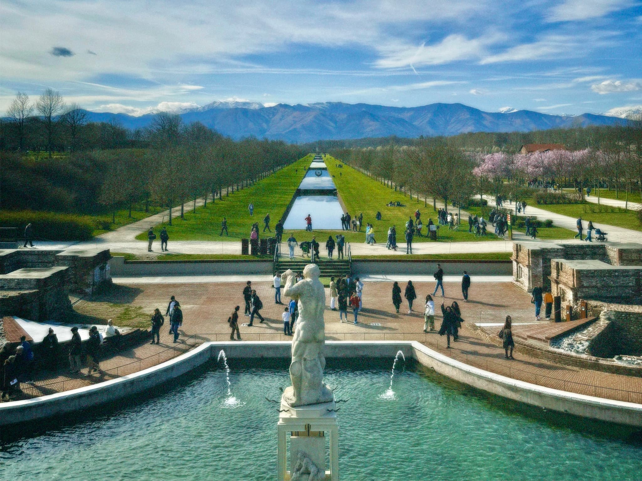 A majestic fountain frames the sweeping lawns and rolling hills of a grand chateau, bathed in soft spring light, evoking a serene and luxurious ambiance