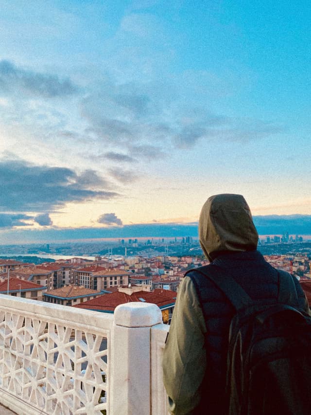 Person gazes at a stunning cityscape at dawn, with soft blue skies and scattered clouds, creating a serene and contemplative atmosphere