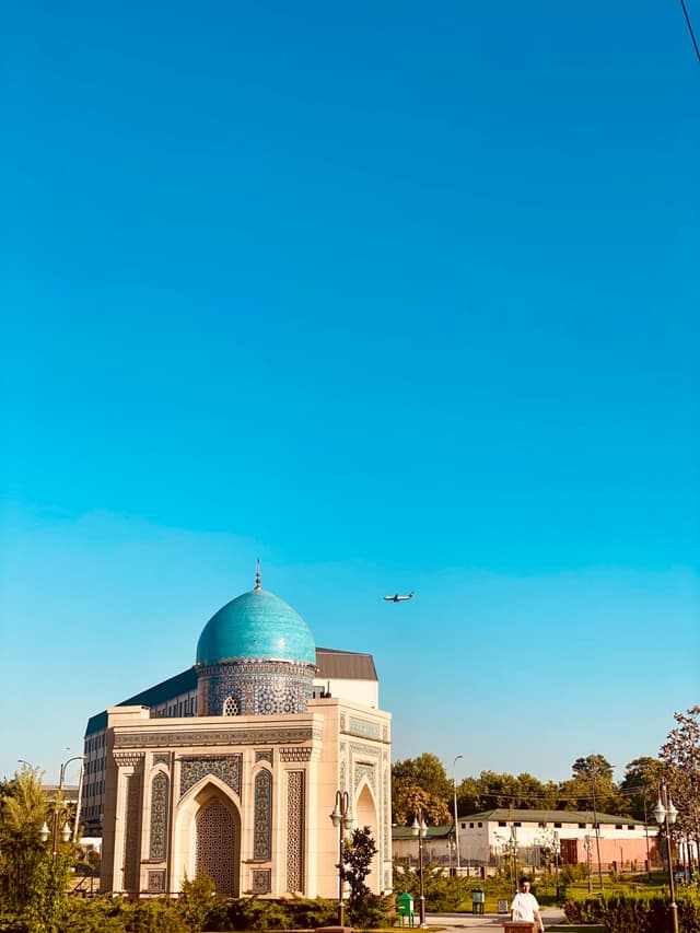 A serene blue dome contrasts against a clear sky, bathed in soft morning light; quiet cobblestone houses and greenery surround the historic Islamic architecture