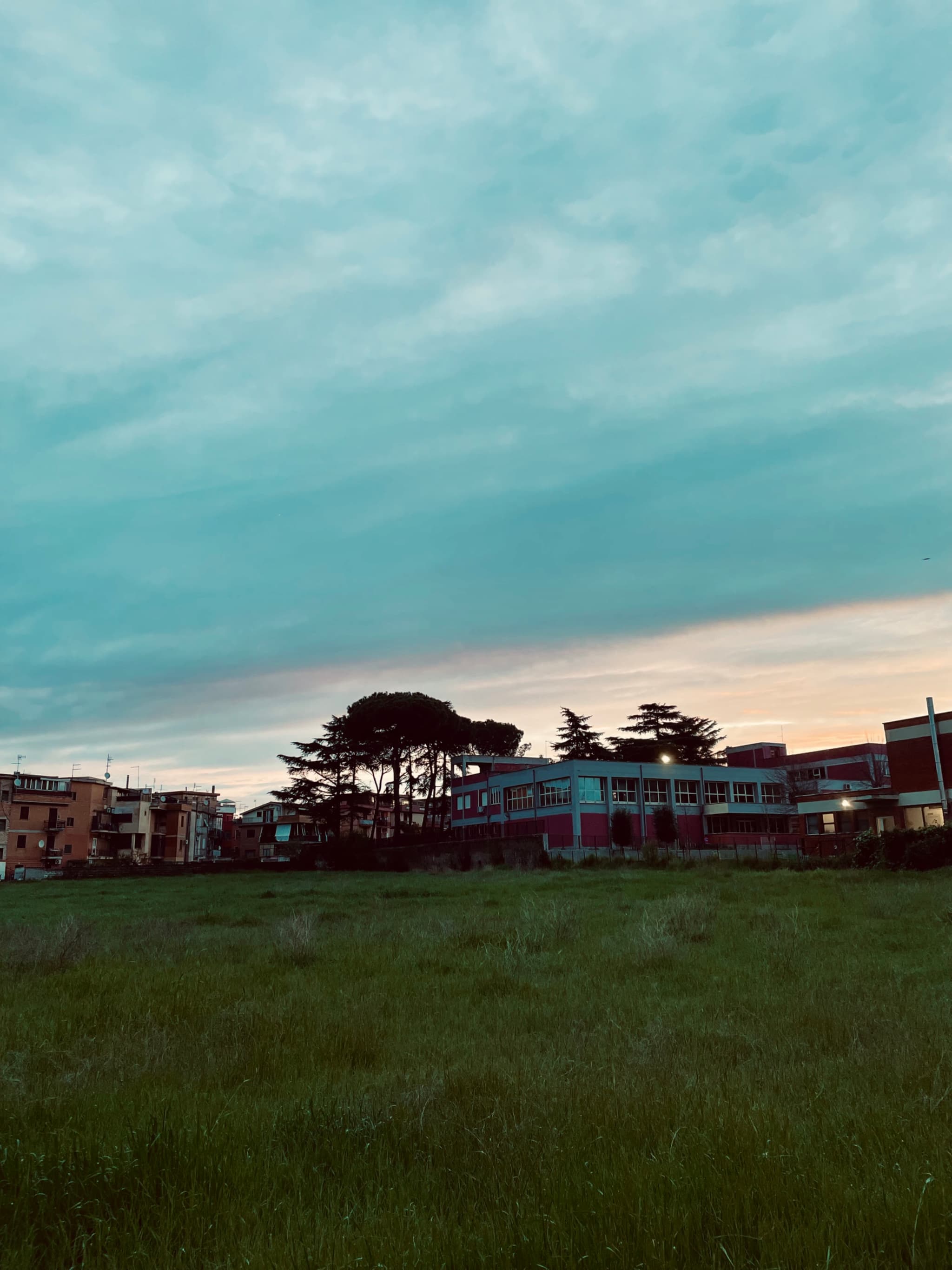 A serene twilight scene with a grassy field, silhouetted buildings, and a sky transitioning from soft blues to warm oranges, evoking calm and quiet