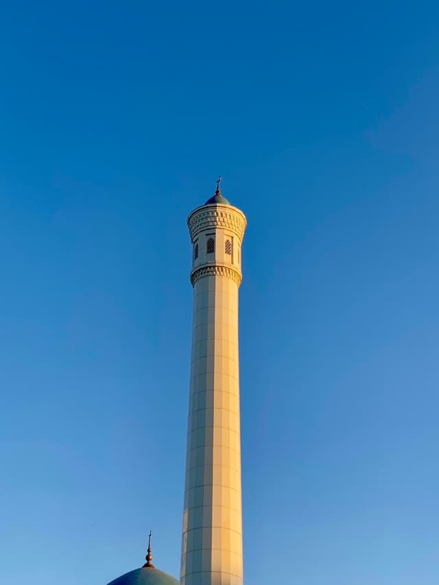 A majestic minaret stands tall against a clear blue sky, bathed in warm evening light, creating a serene and majestic atmosphere