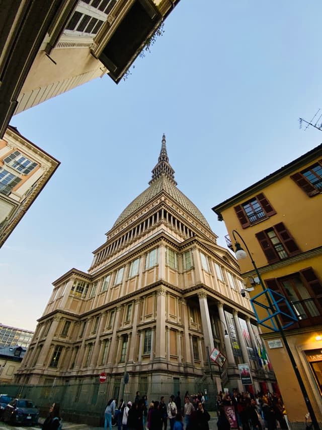 A historic, ornate building with a tower stands under a clear sky, illuminated by warm streetlights, creating a serene, inviting atmosphere in a bustling urban setting