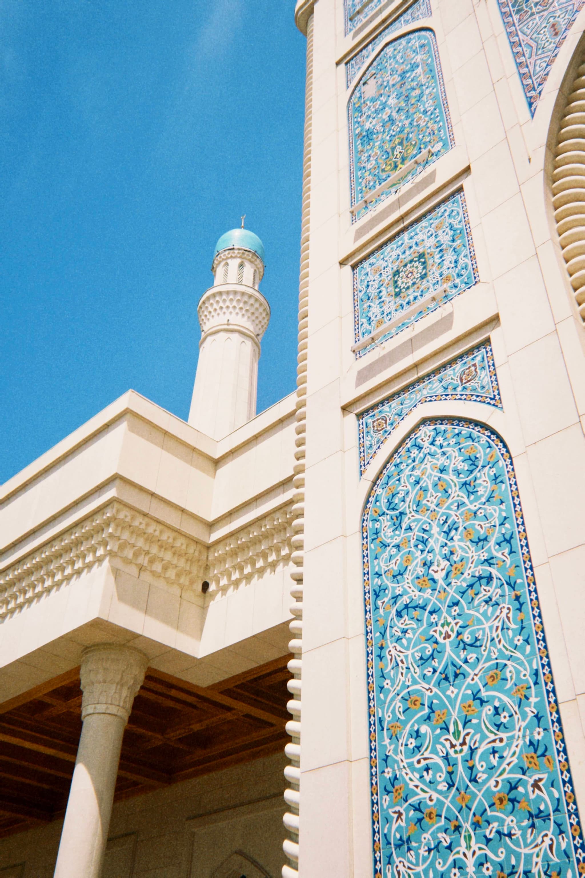 Elegant mosque architecture with intricate blue tiles, white columns, and a blue dome against a bright blue sky, evoking a serene and spiritual atmosphere