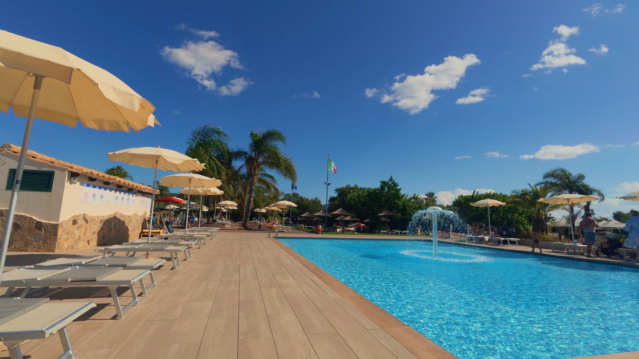 A bright, sunny day by a sparkling pool with lounge chairs, umbrellas, and palm trees, exuding a relaxing, tropical vibe