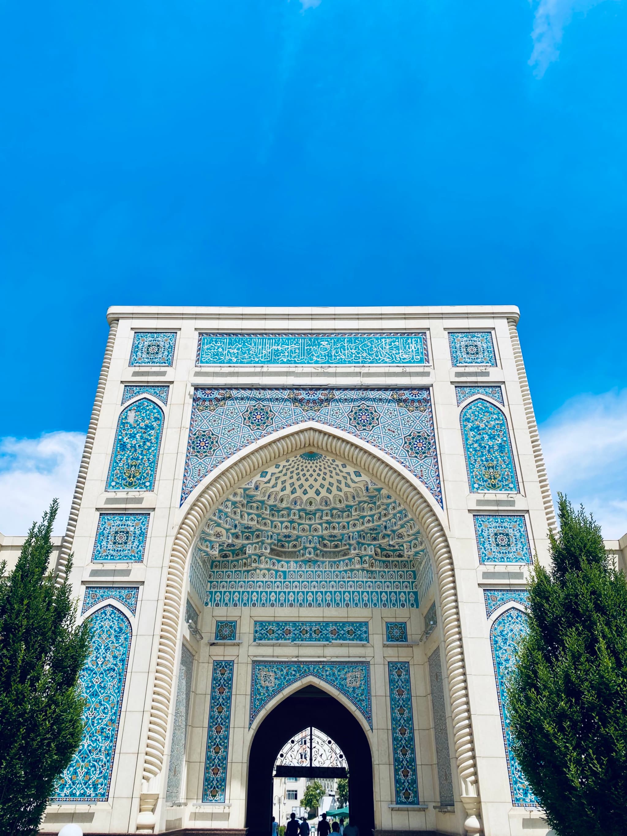 A stunning mosque entrance under a vivid blue sky, illuminated by bright sunlight, evoking a serene and majestic atmosphere