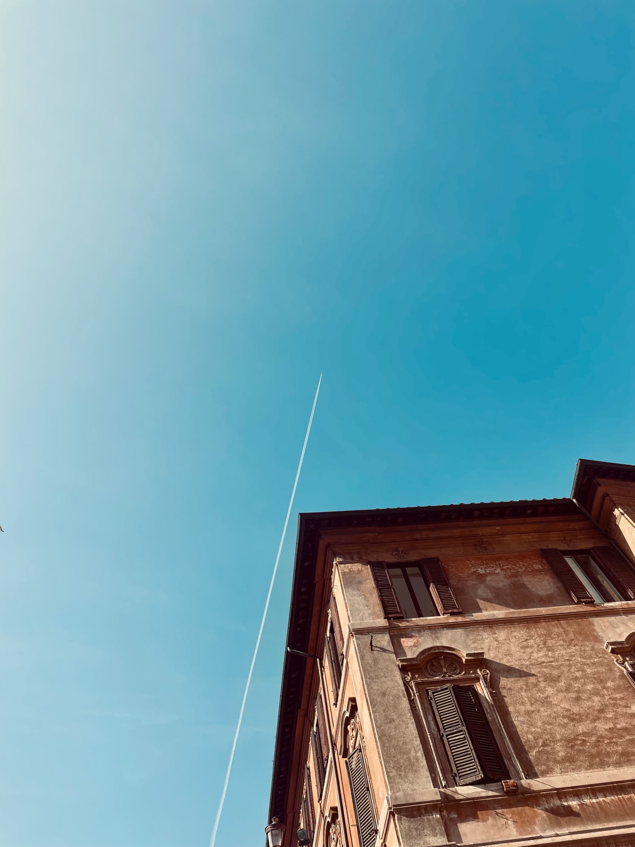 A striking upward view of an old brick building against a clear blue sky, with a thin wire stretching across, evoking a sense of tranquility and nostalgia