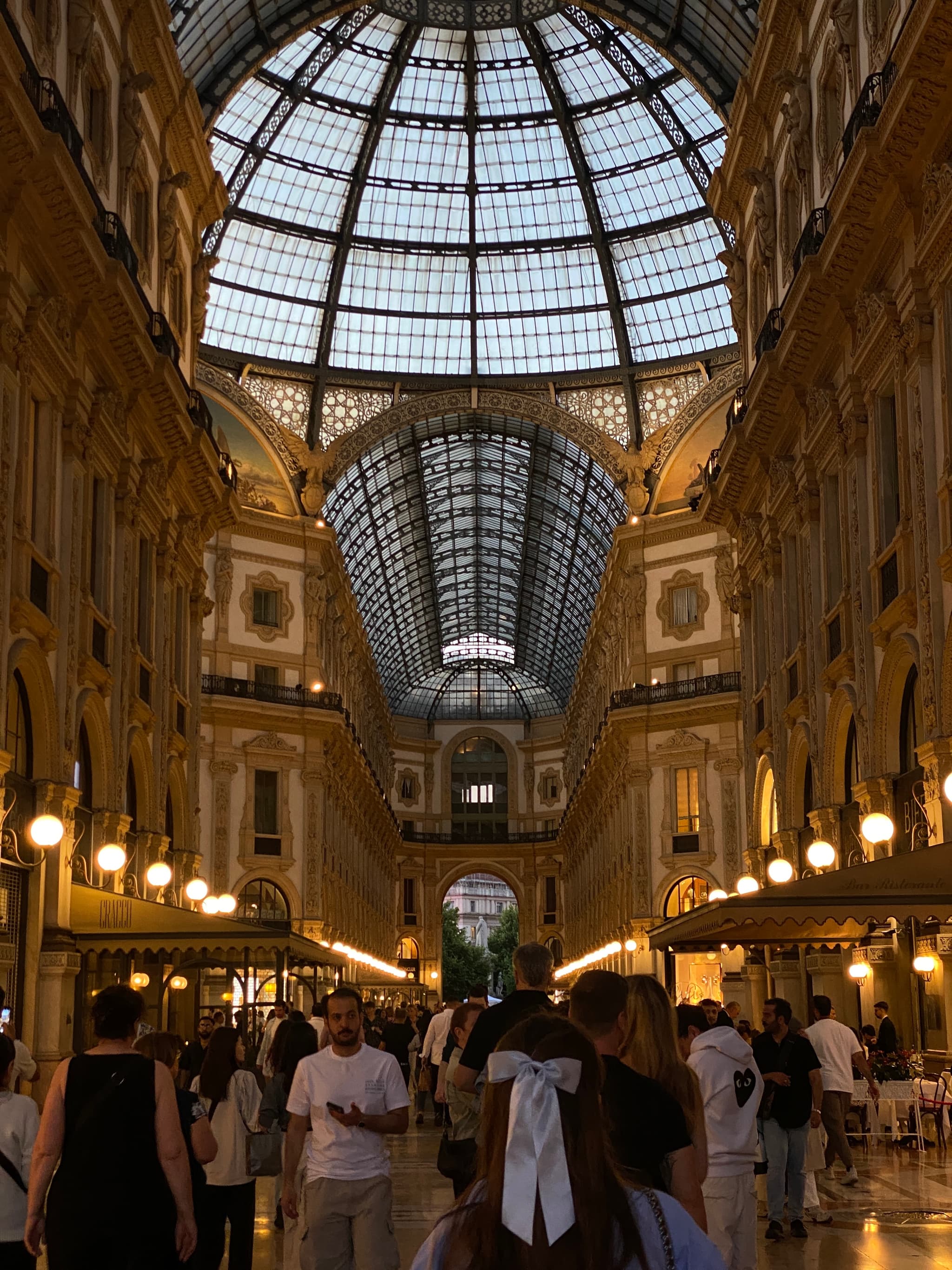 Grand shopping arcade with glass dome, warm lighting, bustling crowd, and elegant architecture
